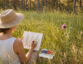 Une femme dessine à l'aquarelle dans une forêt