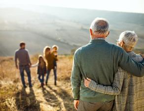 Au 1er plan un couple de personnes âgées enlacées de dos regarde au loin un jeune couple avec 2 enfants