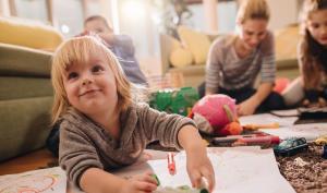 Des enfants parterre en train de dessiner sur des pages sous la surveillance d'une nounou