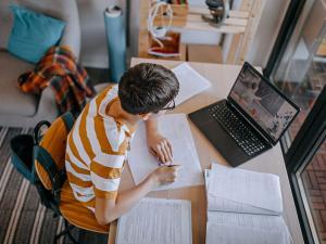 Un adolescent faisant ses devoirs devant son ordinateur dans sa chambre