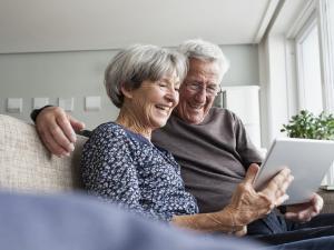 Une femme et un homme âgés sourient et utilisent une tablette