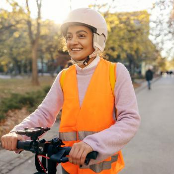 Une femme avec un casque et un gilet rétro-réfléchissant sur une trottinette électrique