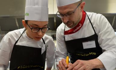 Un cuisinier montre un geste pro à une apprentie