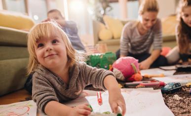 Des enfants parterre en train de dessiner sur des pages sous la surveillance d'une nounou