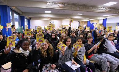 Des collégiens réunis dans une salle brandissent leur attestation scolaire de sécurité routière