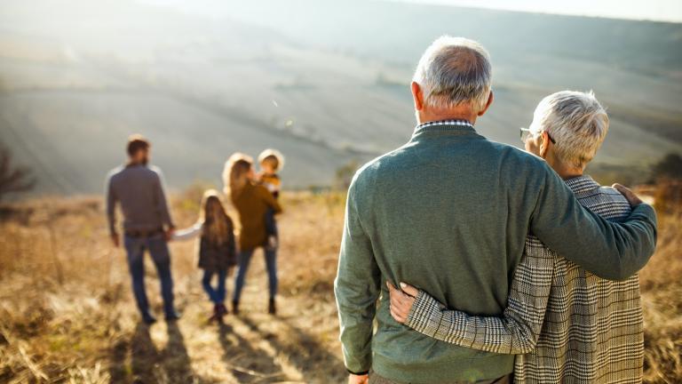 Au 1er plan un couple de personnes âgées enlacées de dos regarde au loin un jeune couple avec 2 enfants