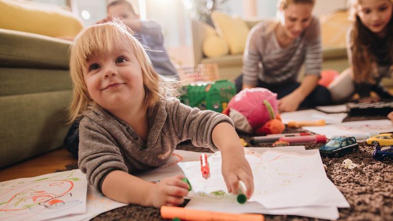 Des enfants parterre en train de dessiner sur des pages sous la surveillance d'une nounou