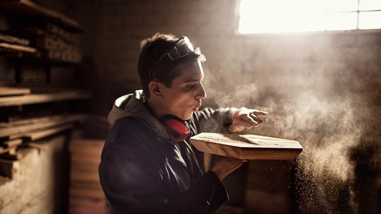 Un jeune artisan du bois souffle sur une pièce qu'il vient de terminer