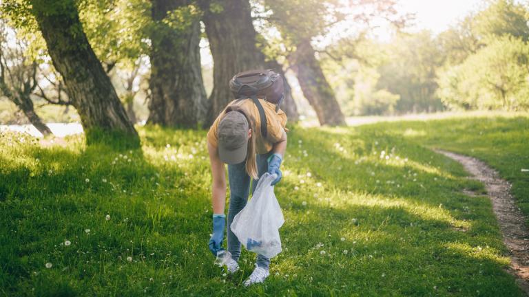 Une femme ramasse un déchet dans une forêt