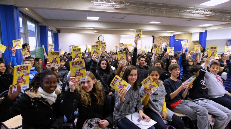 Des collégiens réunis dans une salle brandissent leur attestation scolaire de sécurité routière