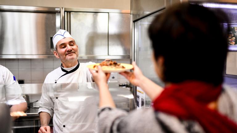 Un cuisinier sert un plat à la cantine