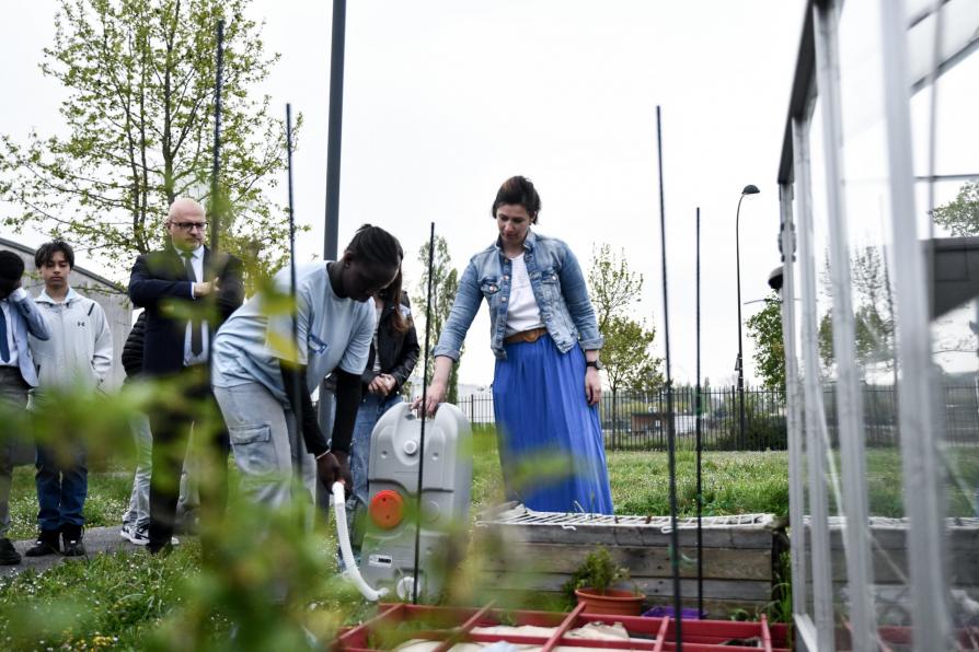 Un collégien arrose un potager à l'aide d'un récupérateur d'eau