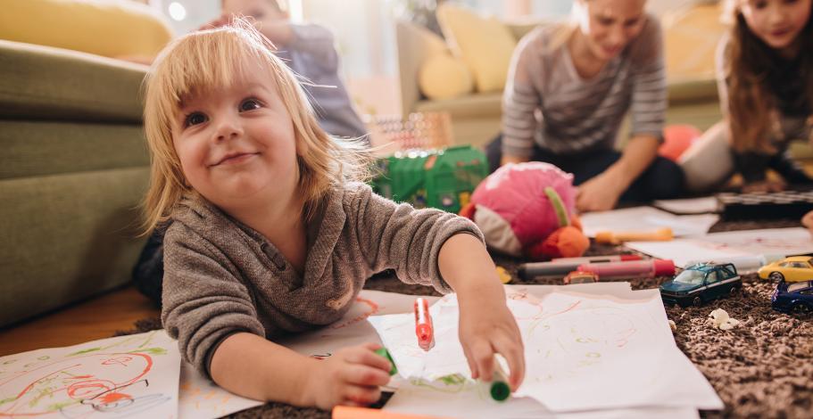 Des enfants parterre en train de dessiner sur des pages sous la surveillance d'une nounou