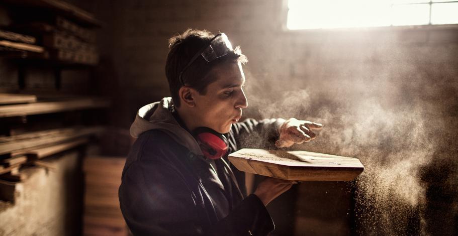 Un jeune artisan du bois souffle sur une pièce qu'il vient de terminer